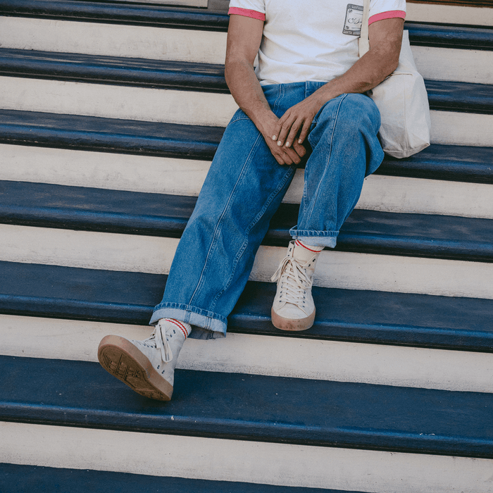 Person sitting on a set of outdoor stairs wearing jeans and beige high-top sneakers.