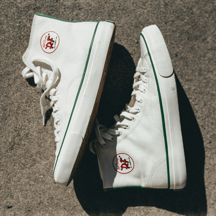 White high-top sneakers with green accents on a concrete surface.