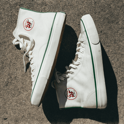 White high-top sneakers with green accents on a concrete surface.