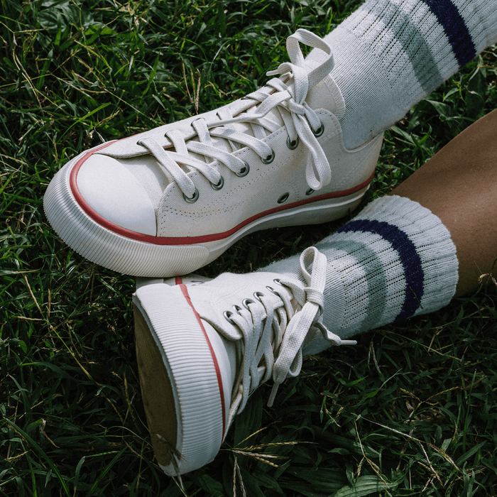 Close-up of white low-top sneakers with crimson accents, worn with white ankle socks on grass.
