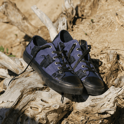Pair of blue sneakers with black soles on a wooden log