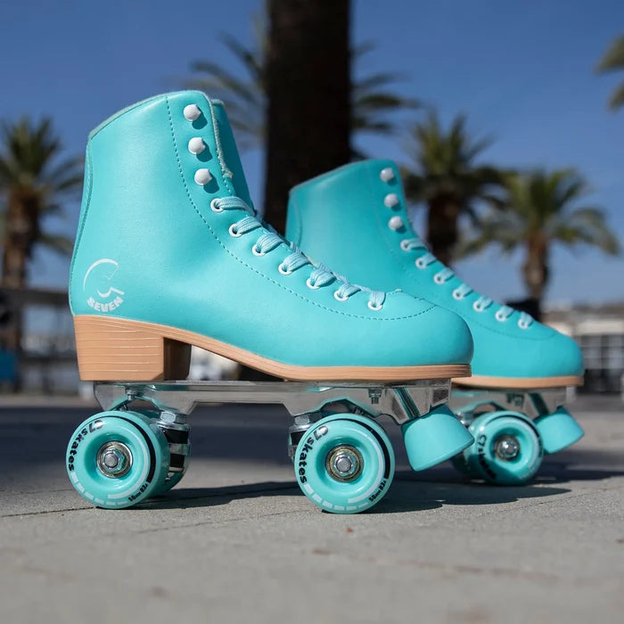 Pair of turquoise roller skates with clear wheels on a pavement background.