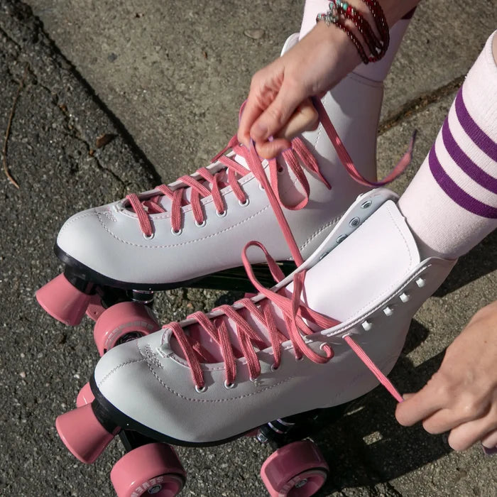 White roller skates with pink laces and wheels on a concrete surface