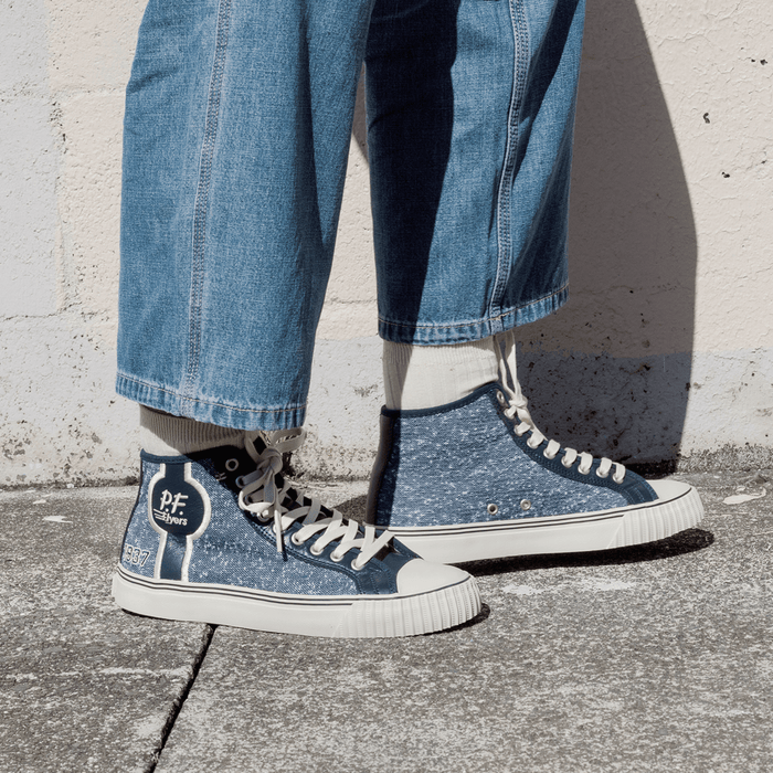 Navy jersey-textured high-top sneakers worn with jeans, standing against a concrete wall.