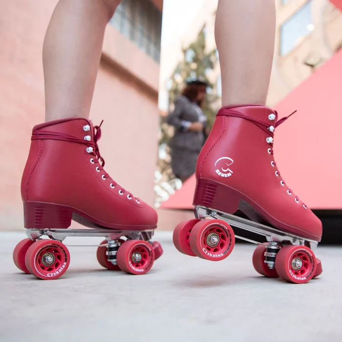 Red roller skates with pink wheels worn by a person on a light surface.