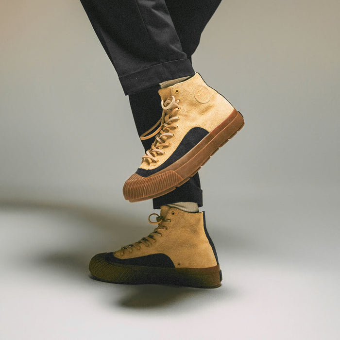 Tan high-top sneakers with gum soles worn by a person on a neutral background