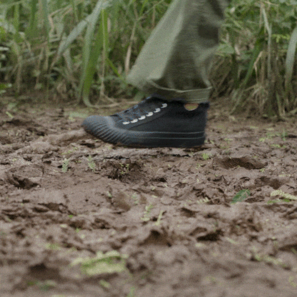 Person wearing black high-top sneakers and green pants on a muddy hiking trail.