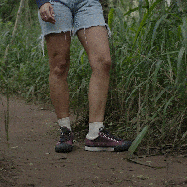 Person hiking a muddy trail wearing burgundy low-top sneakers with black accents.