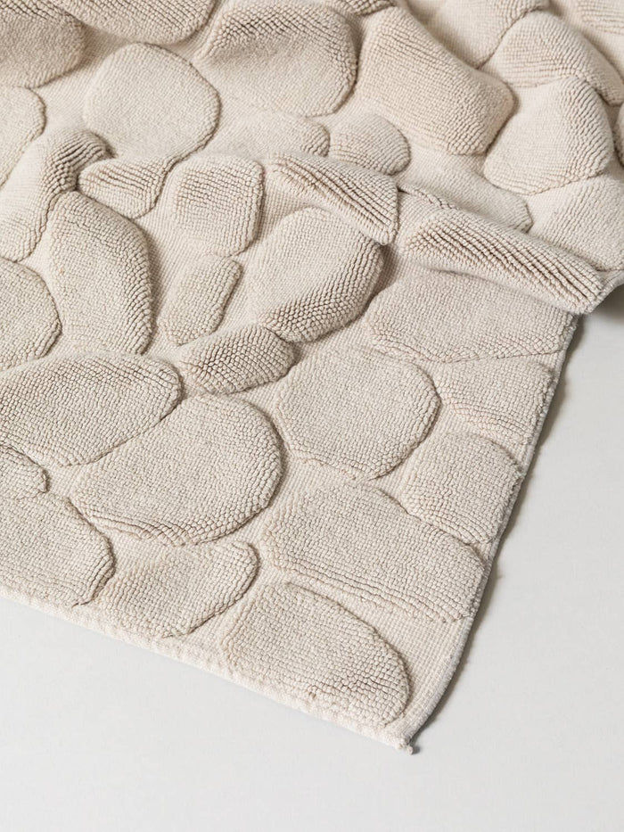 Textured beige bath mat with raised patterns on a light gray background