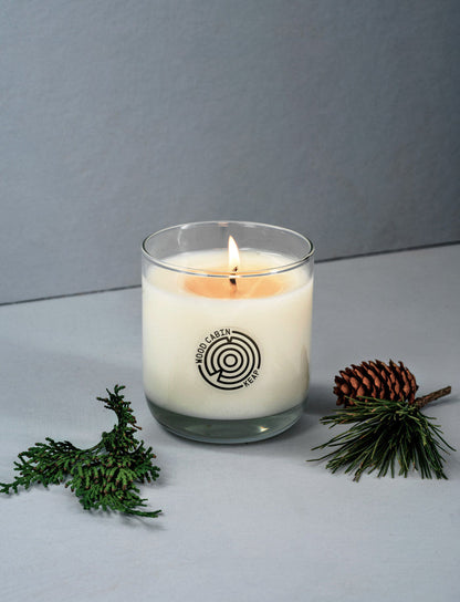 Candle in a glass jar with a logo, surrounded by greenery on a gray background