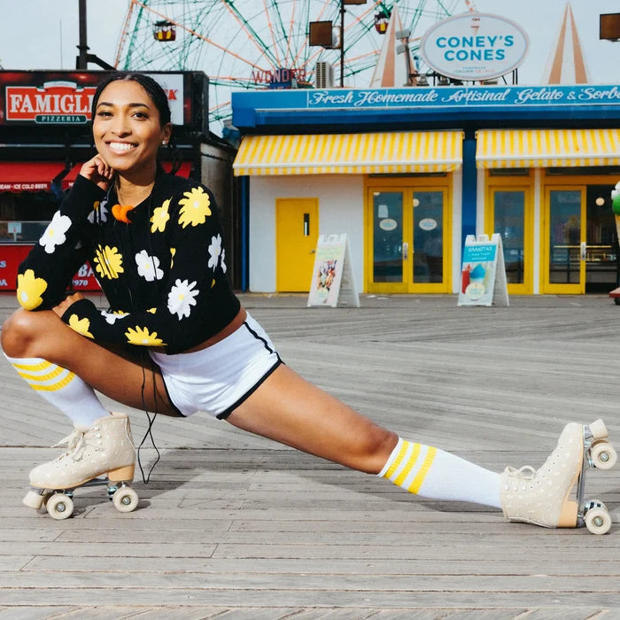 Woman in a floral outfit with roller skates on a boardwalk with a Ferris wheel in the background.