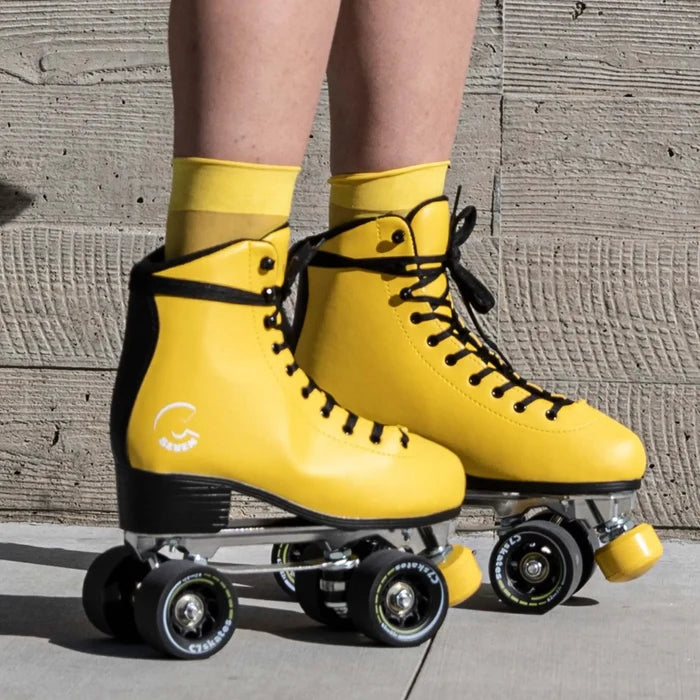 Yellow roller skates with black wheels worn by a person against a concrete wall.
