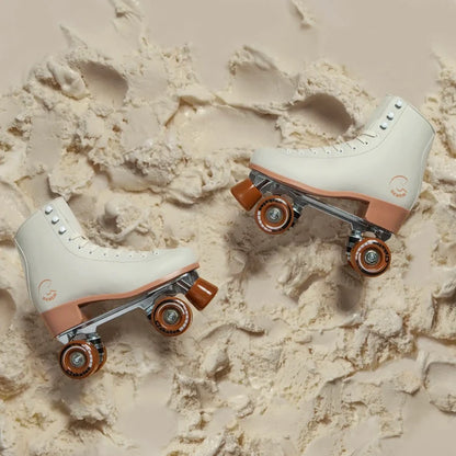Pair of white and brown roller skates on a textured beige surface